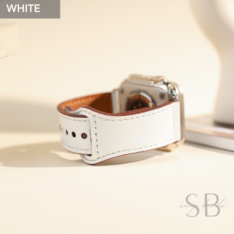 White leather Apple Watch band with brown leather accents. The band has a buckle closure and is designed for the Apple Watch.