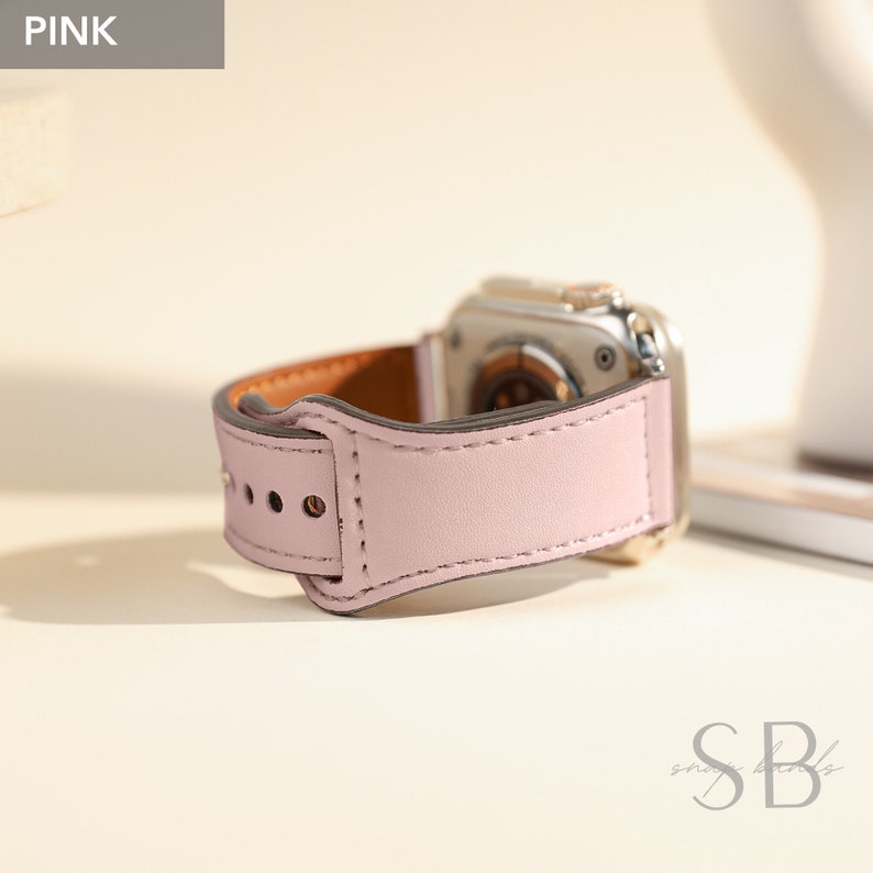 A pink leather watch band with a silver watch face. The band has a stitched design and a buckle closure.