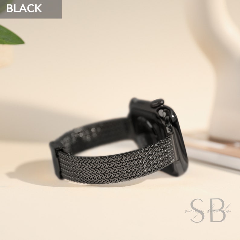 A black smartwatch with a woven metal band. The watch face is glossy black, and the band has a textured, mesh-like appearance. The word "BLACK" is in a gray box in the upper left corner.