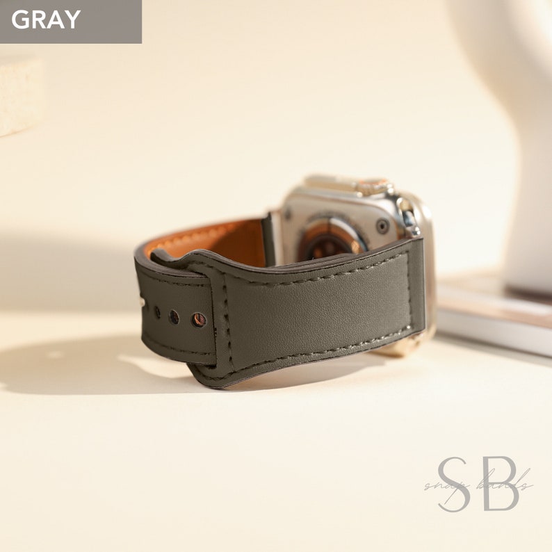 A gray leather watch band with a brown leather lining. The band has a buckle closure and is designed for a smartwatch.