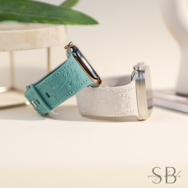 Two Apple Watch bands with floral designs. The band on the left is teal and the band on the right is white.