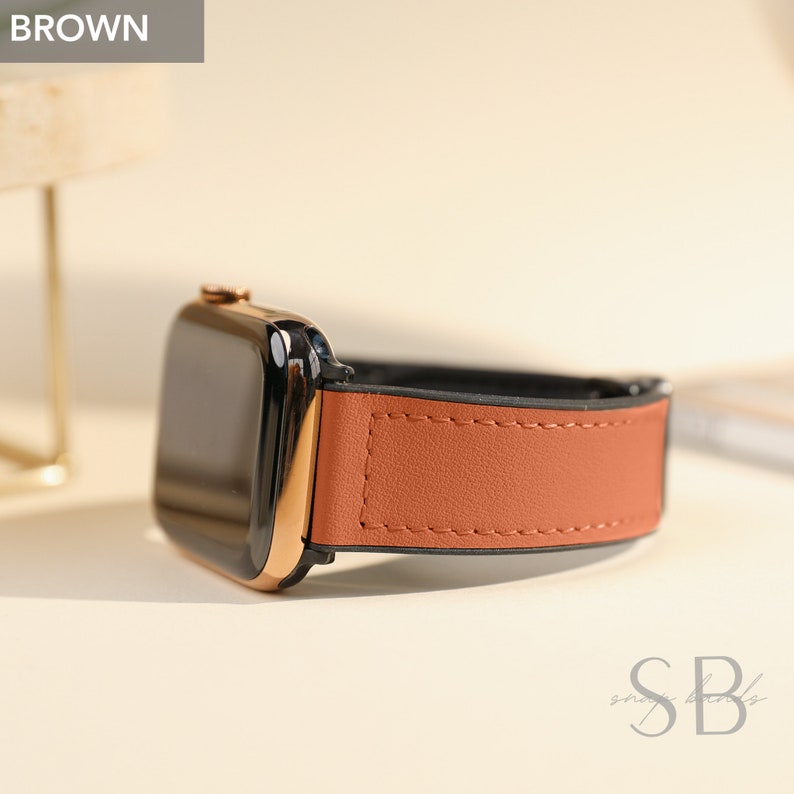 Brown leather watch band attached to a black and gold smartwatch. The band is a warm brown color with a stitched edge. The word "BROWN" is in a white box in the upper left corner.