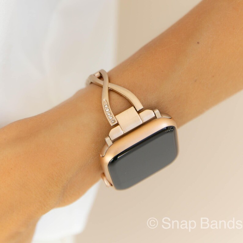 A rose gold Apple Watch band with a crystal-encrusted, interwoven design. The band is shown on a person's wrist.