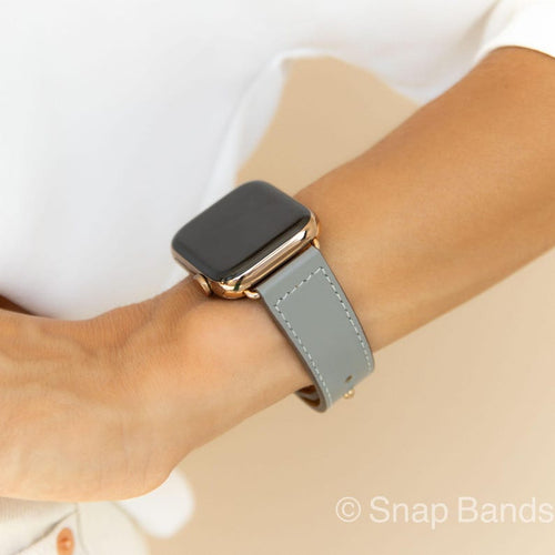 A gray leather watch band with a rose gold Apple Watch. The band has white stitching.