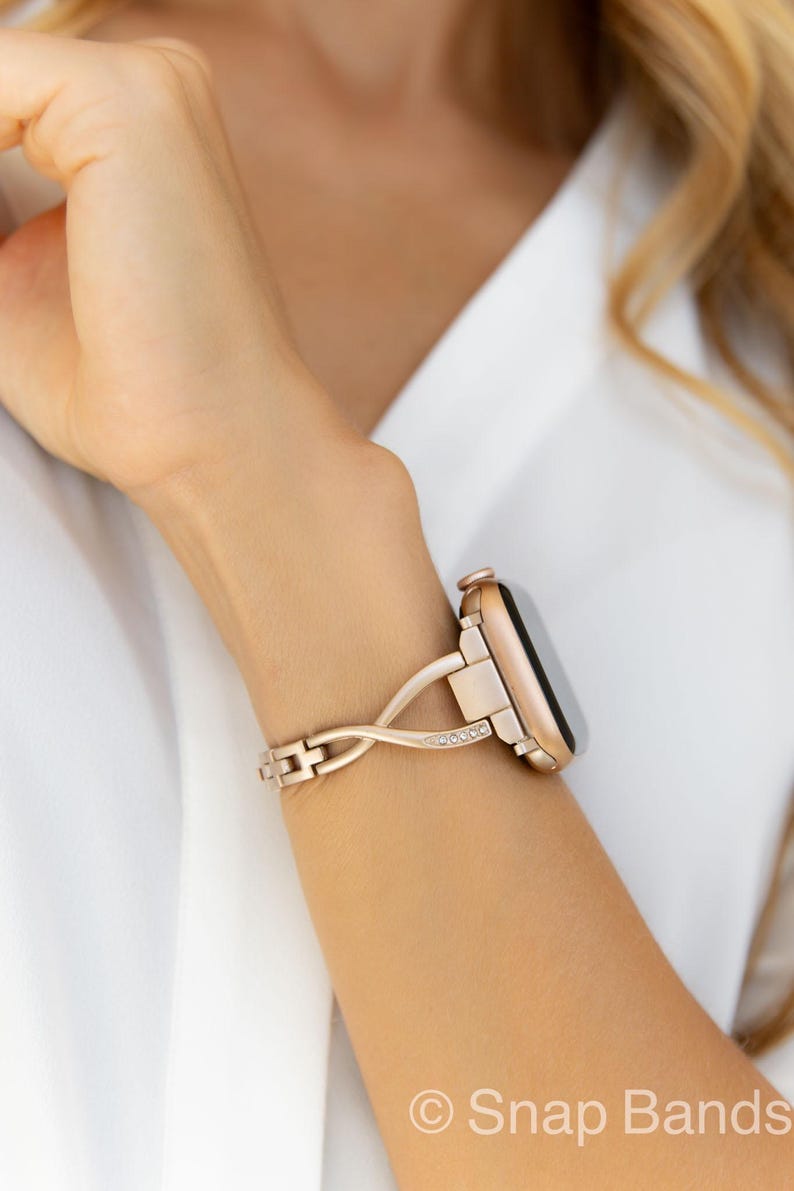 A rose gold Apple Watch band with a twisted design and clear crystal accents. The band is made of metal and has a snap closure.