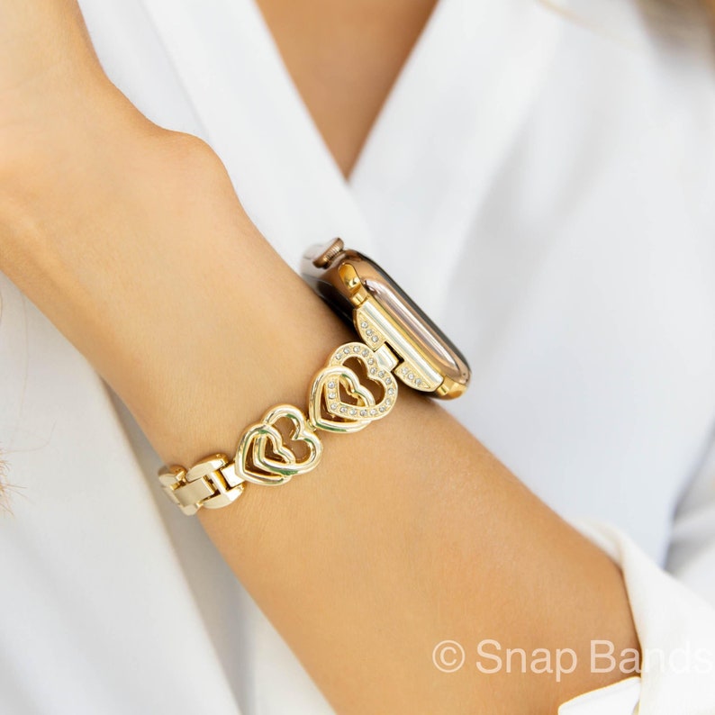Gold watch band with a heart-shaped design and clear rhinestones. The band is compatible with Apple Watch.