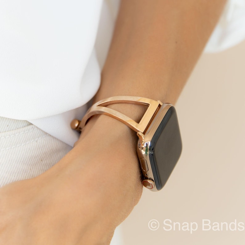 A gold-toned metal watch band with a geometric design. The band is designed to fit a smartwatch.