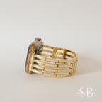 A gold-colored Apple Watch with a matching gold band. The band features a woven design with rectangular links. The watch case has a rose gold finish and a black screen. The watch is displayed on a neutral background.