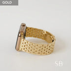 A gold-colored smartwatch with a matching gold metal band. The band is made of rectangular links. The watch face is black. The word "GOLD" is in a gray box in the upper left corner.