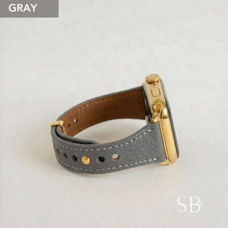 A gray leather watch band with gold-colored hardware. The watch face is gold and the band is stitched with white thread. The word "GRAY" is in a gray box in the upper left corner.
