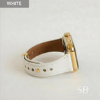 A white leather watch band with gold-colored hardware is shown. The watch face is gold and black. The band is secured with gold-colored rivets. The word "WHITE" is in the upper left corner.