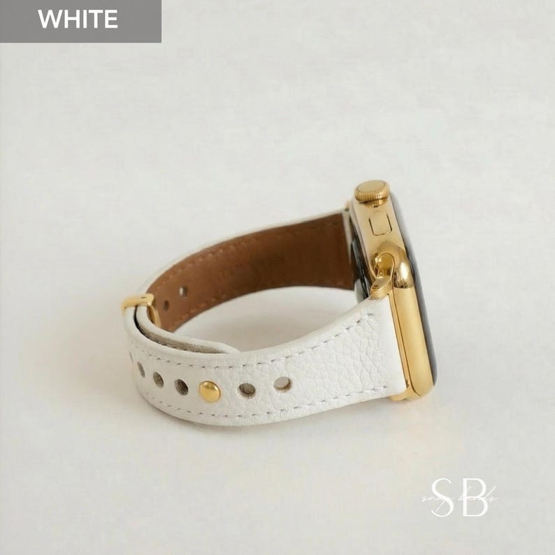 A white leather watch band with gold-colored hardware is shown. The watch face is gold and black. The band is secured with gold-colored rivets. The word "WHITE" is in the upper left corner.