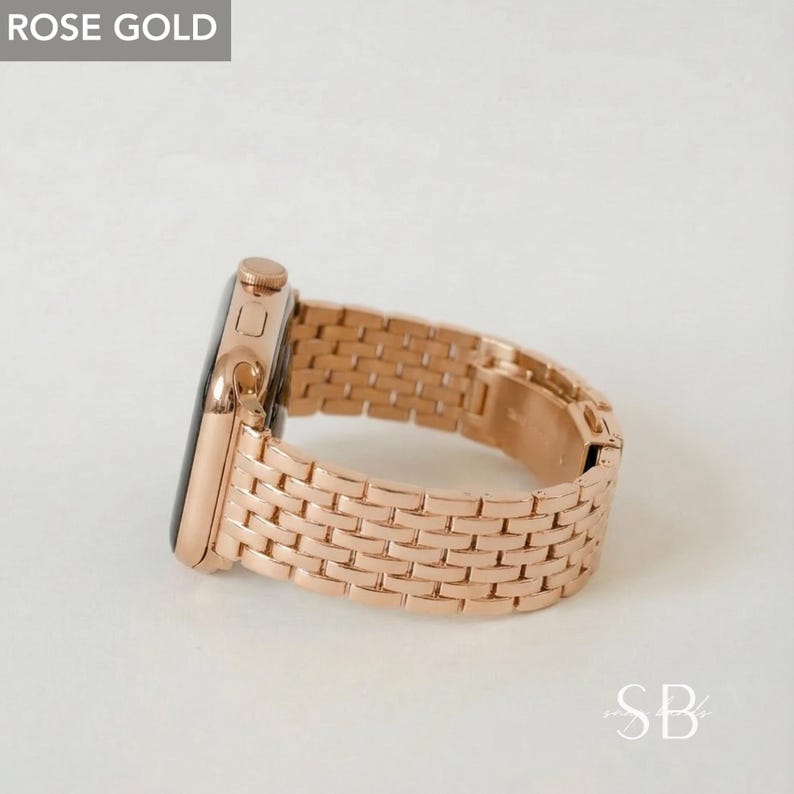 Rose gold smartwatch with a matching band. The band is made of small, rectangular links. The watch face is black. The text "ROSE GOLD" is in a gray box in the upper left corner. The letters "SB" are in the lower right corner.
