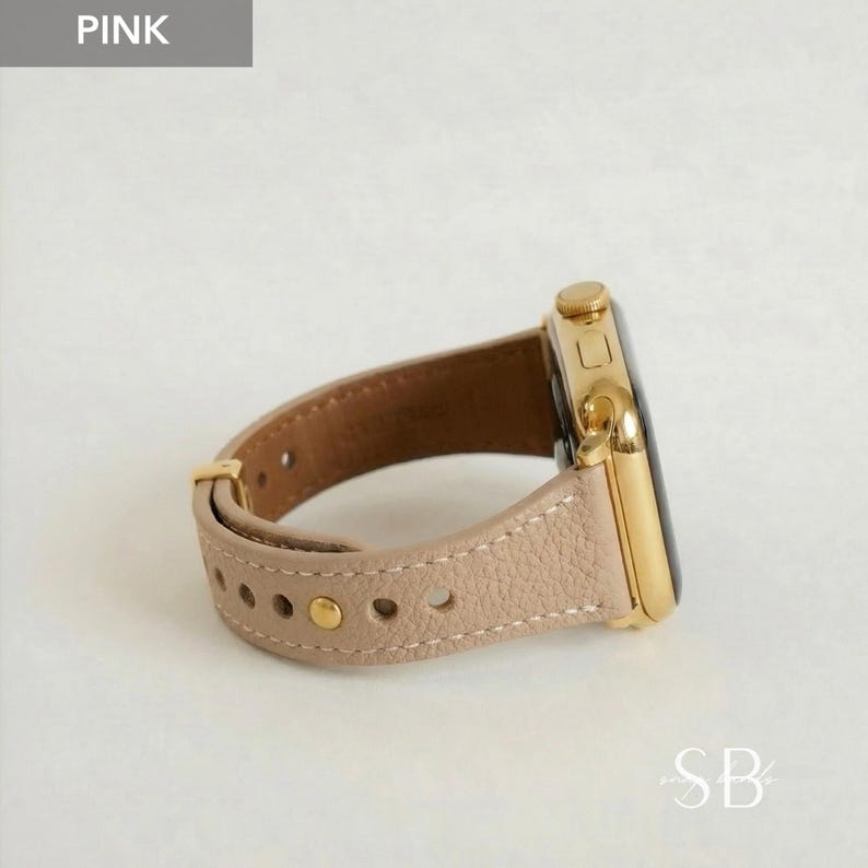 A pink leather watch band with a gold-colored watch face. The band is light pink with gold-colored hardware and a textured surface. The watch face is square with a black screen.