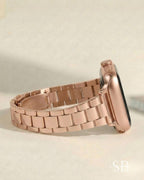 Rose gold smartwatch with a matching metal band. The watch face is black, and the band is made of rectangular links. The watch is shown from a side profile, displaying the crown and the band's clasp.