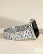 A silver-toned smartwatch with a matching metal band. The watch face is black, and the band is composed of rectangular links. The watch is displayed on a light-colored surface.