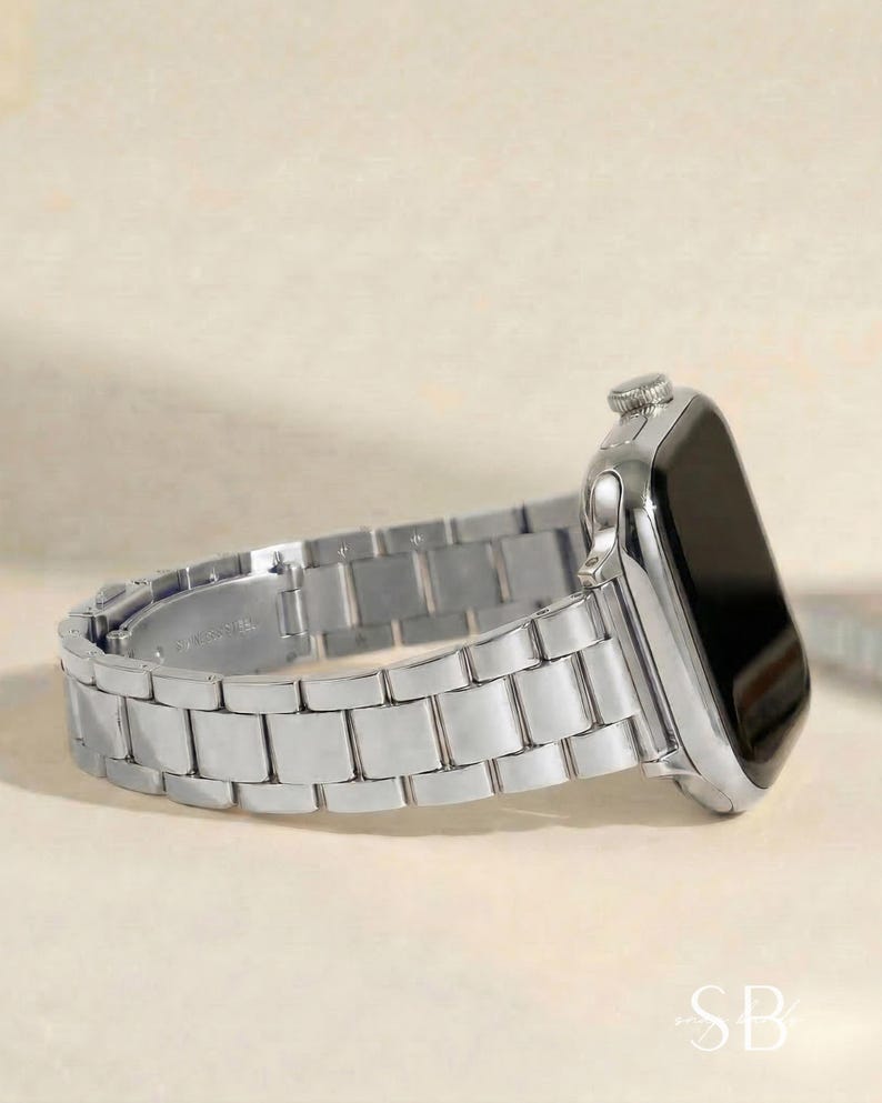 A silver-toned smartwatch with a matching metal band. The watch face is black, and the band is composed of rectangular links. The watch is displayed on a light-colored surface.