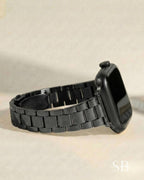 A black smartwatch with a matching black metal band. The band is made of rectangular links. The watch face is black and the crown is visible. The watch is shown on a neutral background.